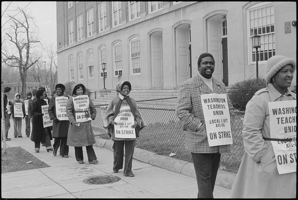 Black teachers carry Washington Teachers Union strike signs in a picket line outside a school.