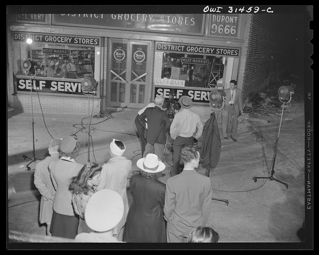 A film crew and onlookers gather outside a Washington grocery store staged for a wartime black-marketing film.