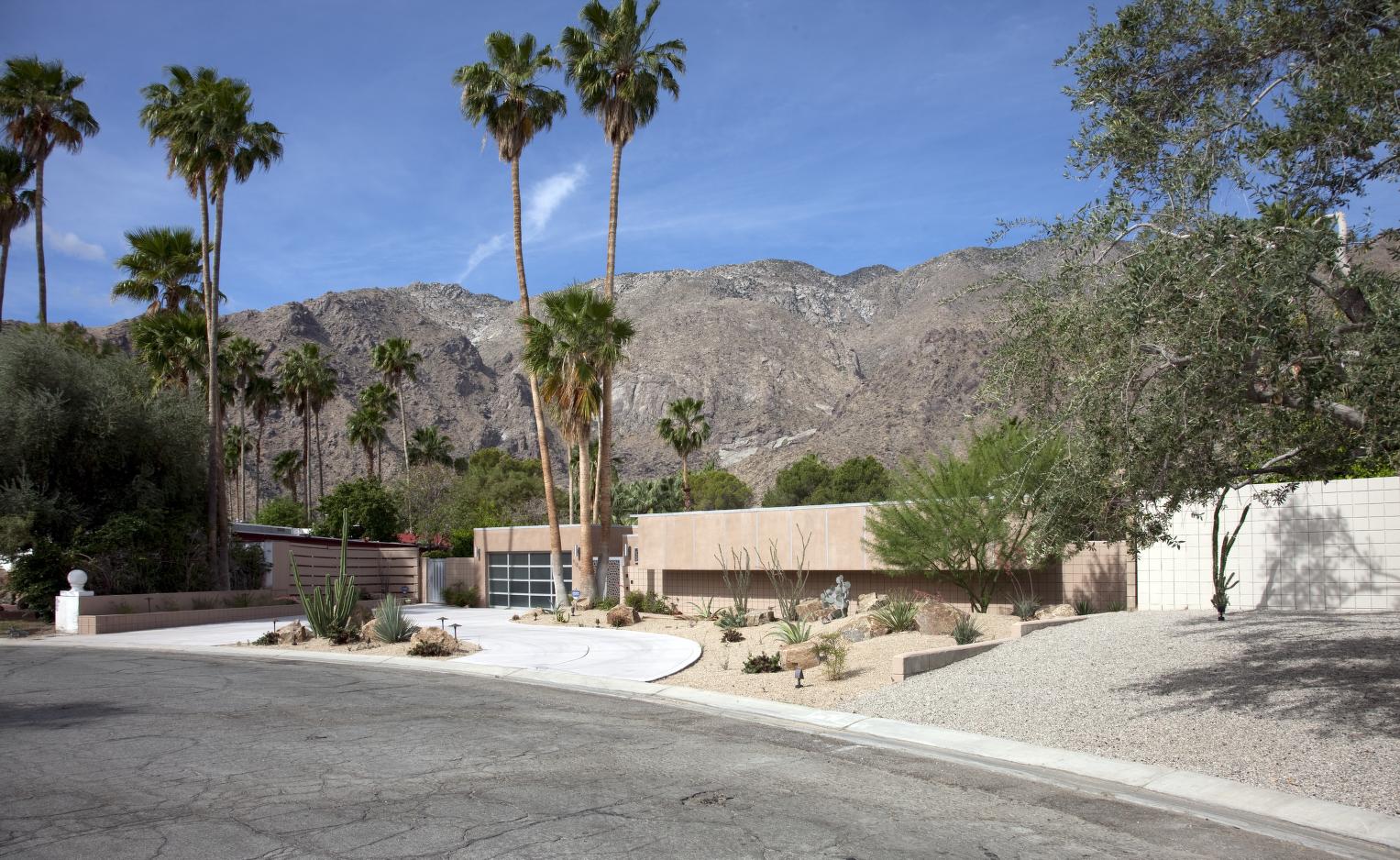 A low mid-century modern house stands against mountains and tall palm trees in Palm Springs, California.